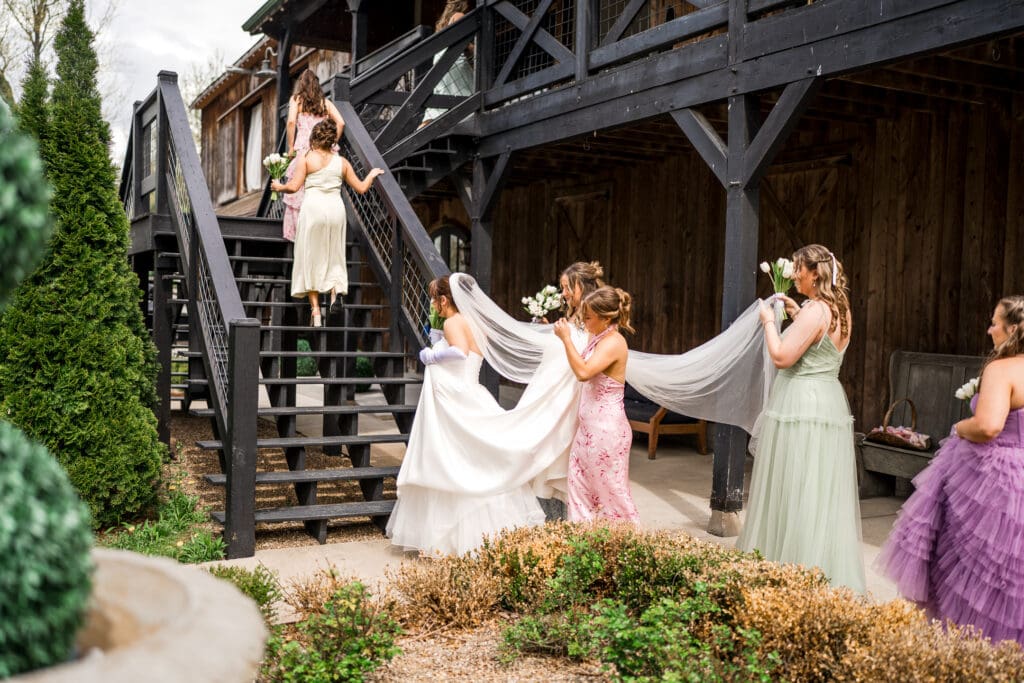 Candid moment as bridesmaids hold the bride's veil at Rivercrest Farms.