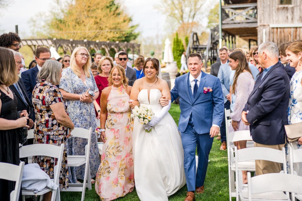 Bride walks down the aisle with her parents at Rivercrest Farms in Dover, Ohio.