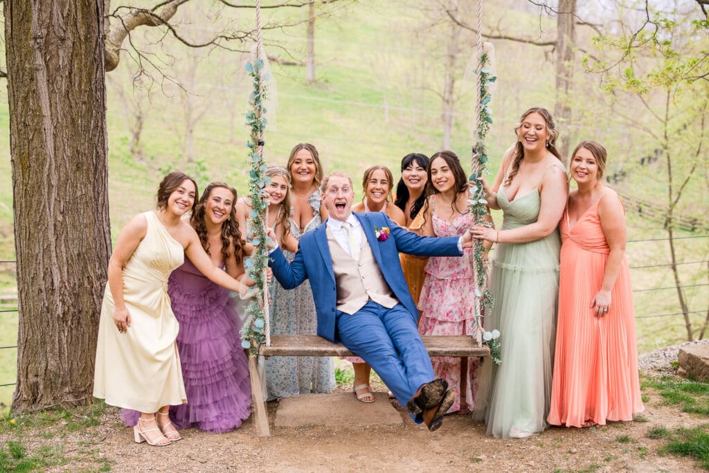 Colorful bridesmaids around the Groom on a swing at Rivercrest Farms.