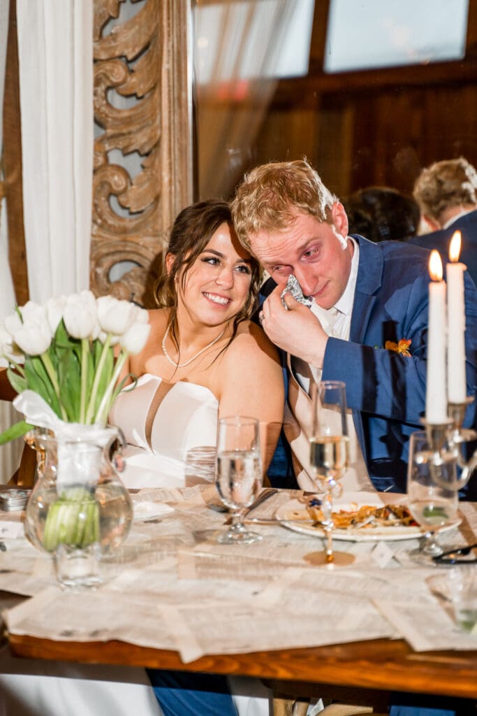 Groom wipes away his tears as his bride watches lovingly during toasts.