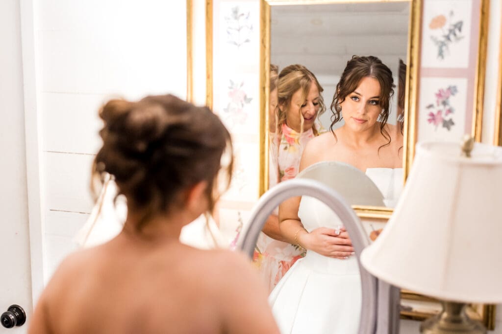 A Bride looks at herself in the mirror while her mom buttons her dress.