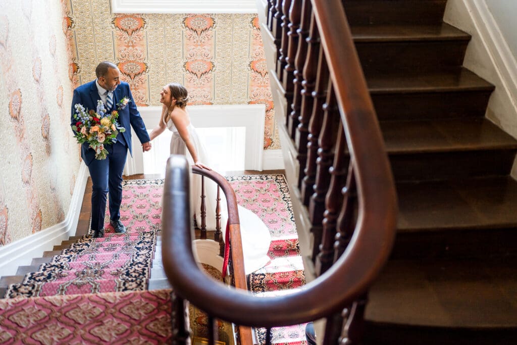 Bride and groom laugh as they walk up the staircase at the Kelton House on their wedding day.