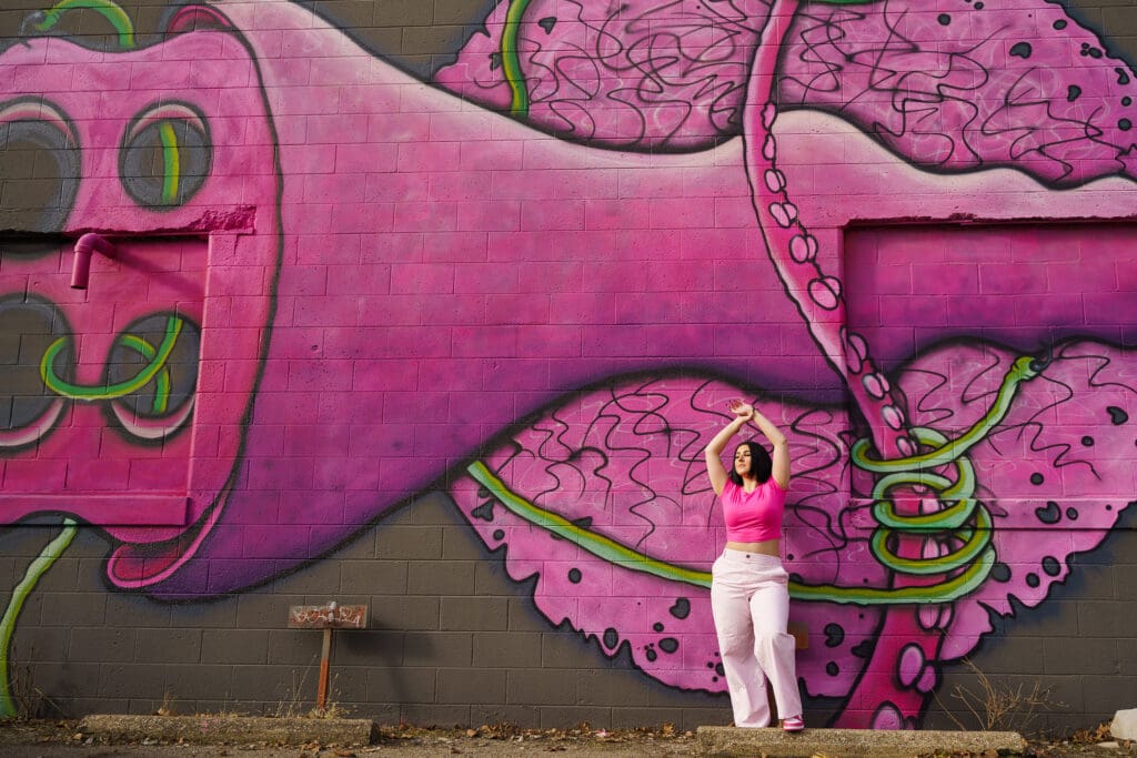Senior in a bright pink outfit by graffiti in Franklinton Columbus, Ohio.