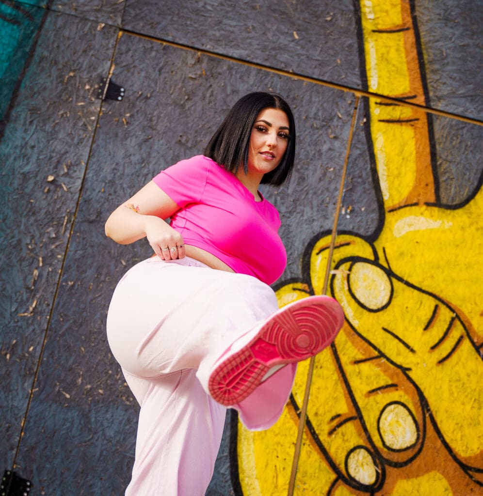 Senior in a bright pink outfit by graffiti in Franklinton Columbus, Ohio.