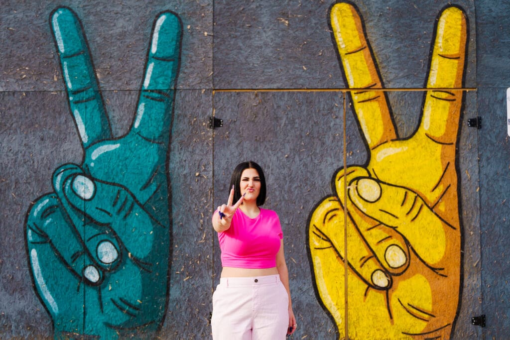 Senior in a bright pink outfit by graffiti in Franklinton Columbus, Ohio.