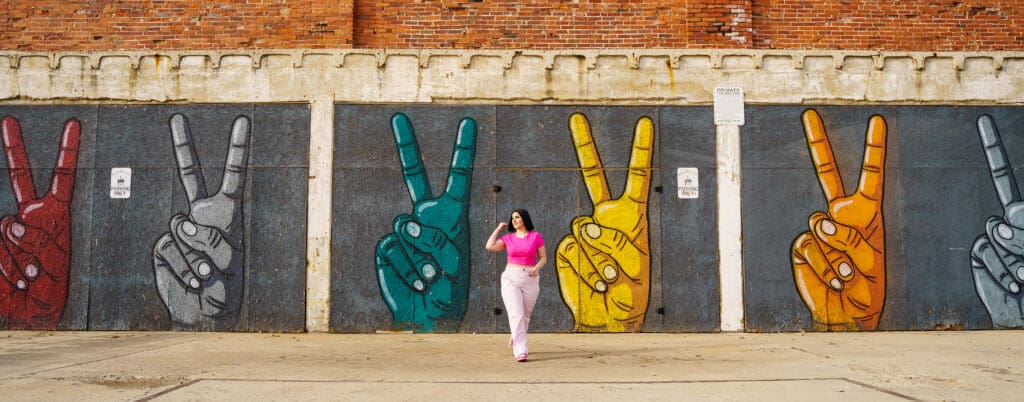 Senior in a bright pink outfit by peace sign graffiti in Franklinton Columbus, Ohio.