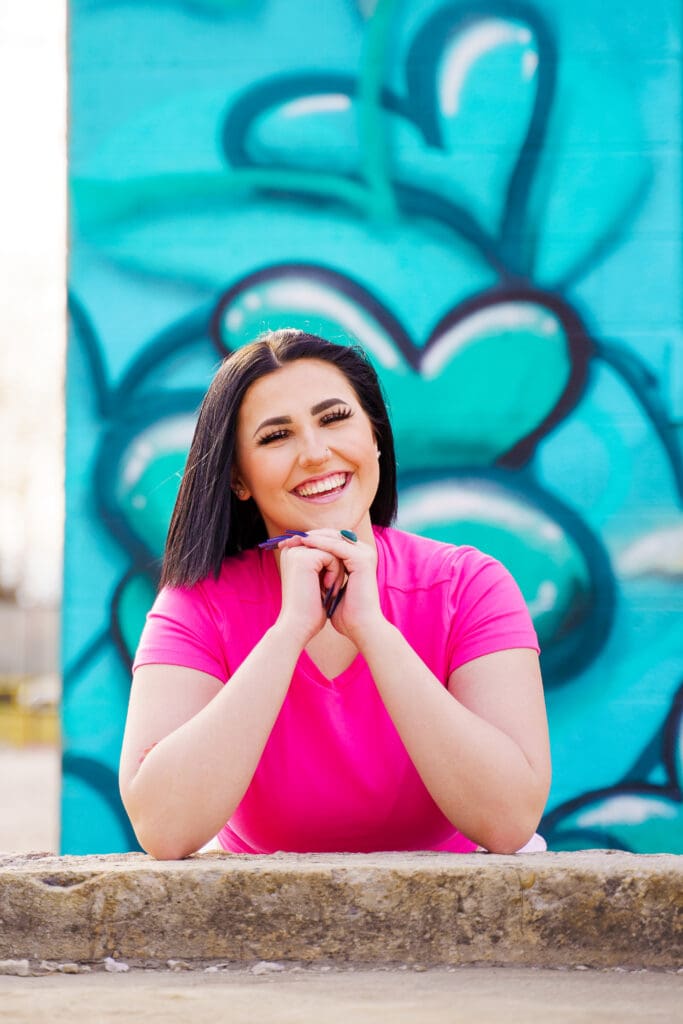 Senior in a bright pink outfit by graffiti in Franklinton Columbus, Ohio.