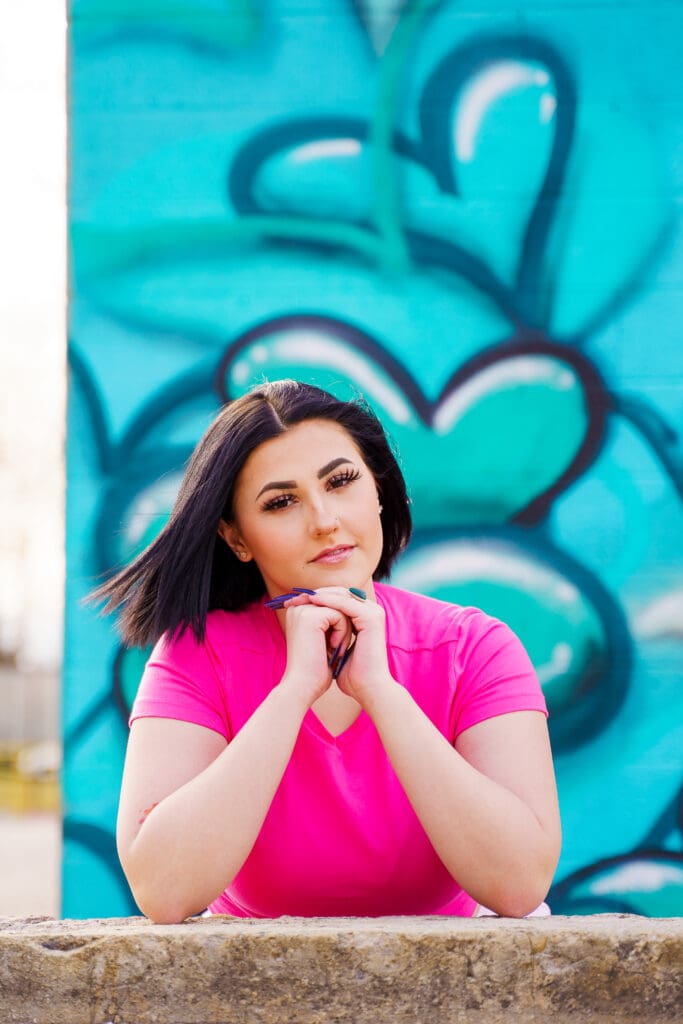 Senior in a bright pink outfit by graffiti in Franklinton Columbus, Ohio.