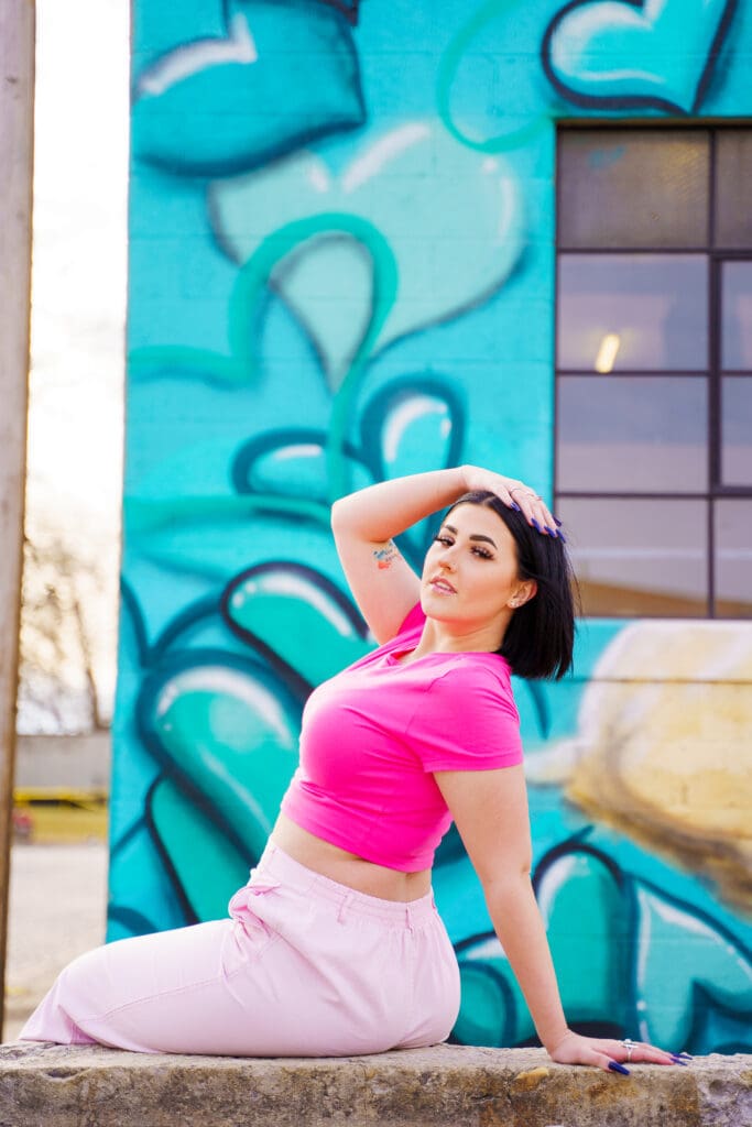 Senior in a bright pink outfit by graffiti in Franklinton Columbus, Ohio.
