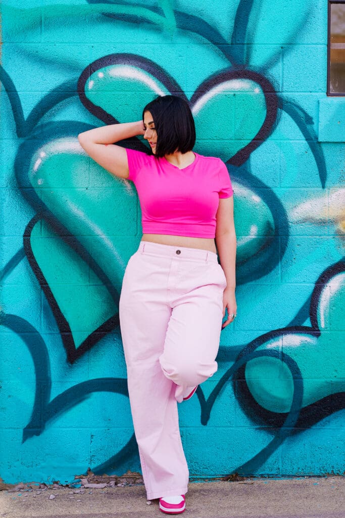 Senior in a bright pink outfit by graffiti in Franklinton Columbus, Ohio.