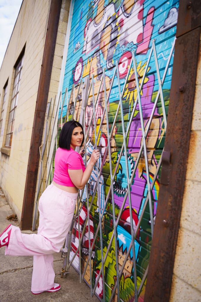 Senior in a bright pink outfit by graffiti in Franklinton Columbus, Ohio.