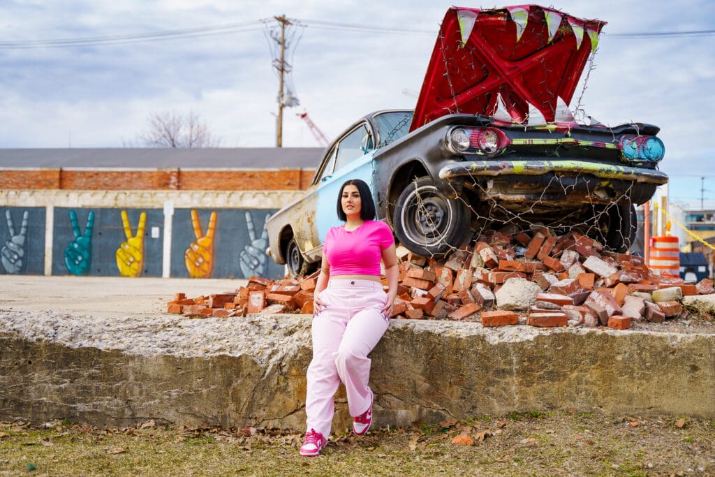 Senior in a bright pink outfit by an artistic car in Franklinton Columbus, Ohio.
