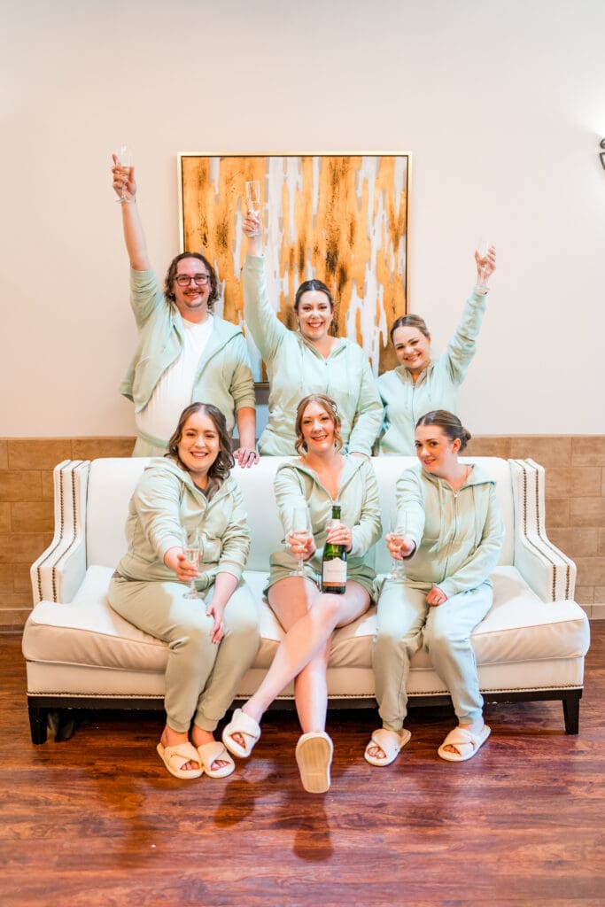 The bride and her wedding party in green sweat suits holding champagne.