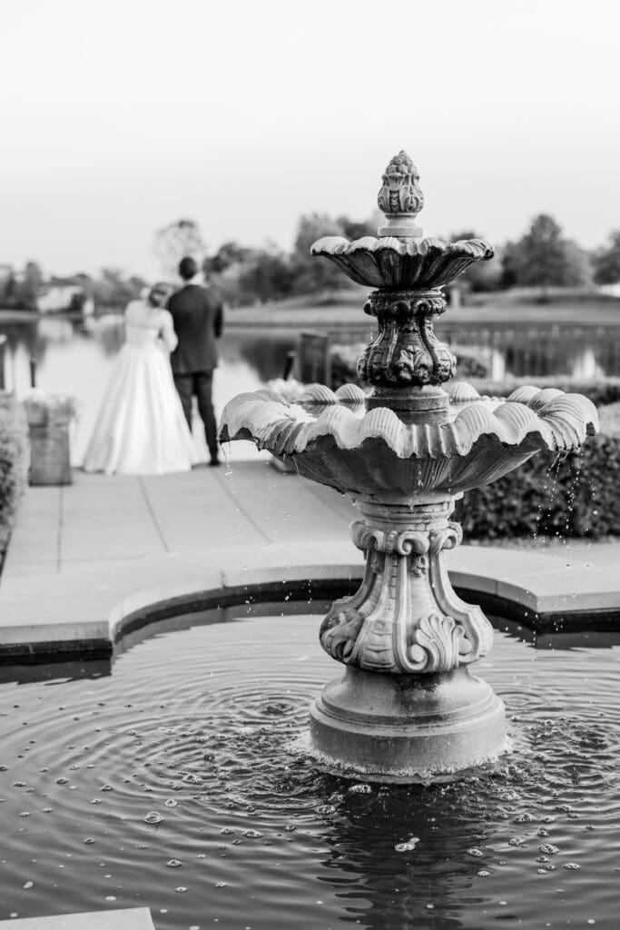 A water fountain and the wedding couple in the background overlooking the lake.