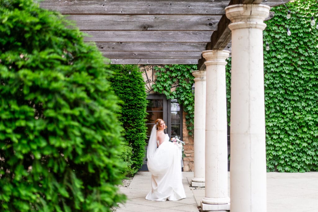 The bride holds her veil and train as she walks and looks back at the camera.