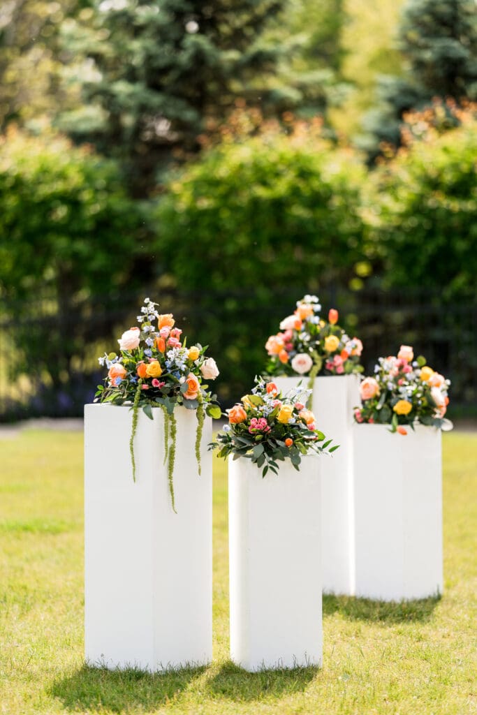 Colorful floral arrangements on top of white pedestals outside.