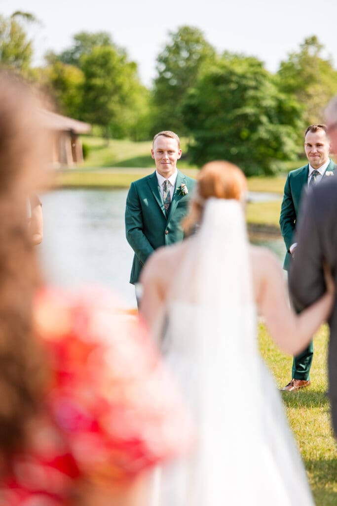 The groom smiles at the bride as she walks down the aisle.