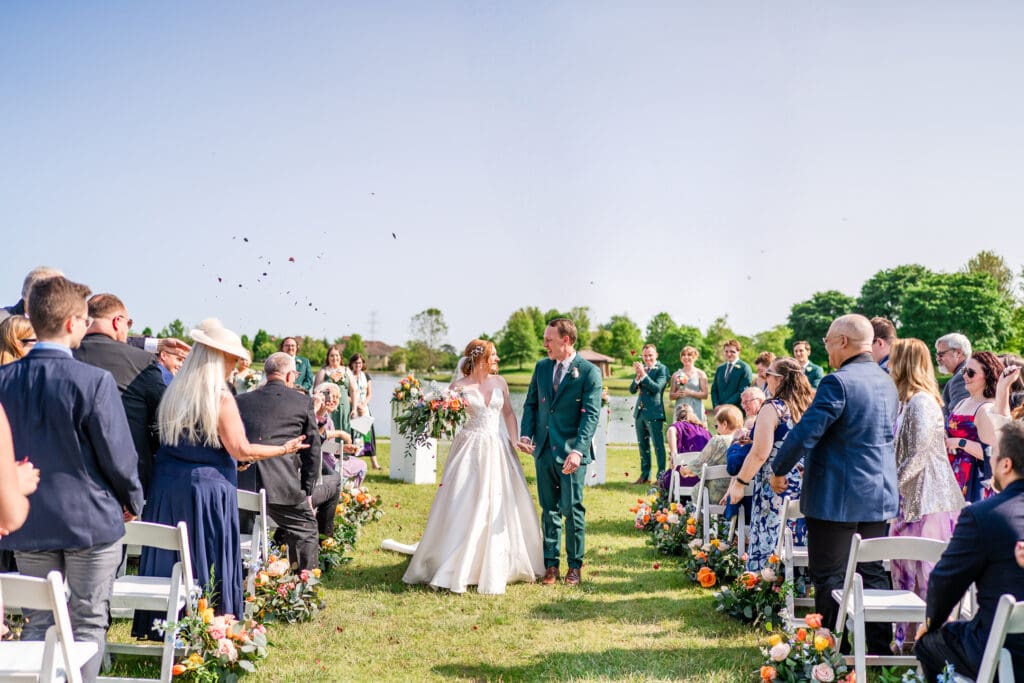 Guests throw flower petals as the bride and groom exit and smile at each other.