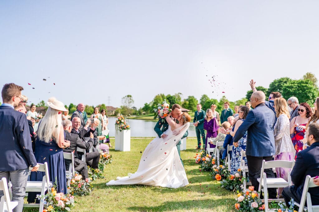 The bride and groom dip kiss in the aisle as guests throw flower petals.