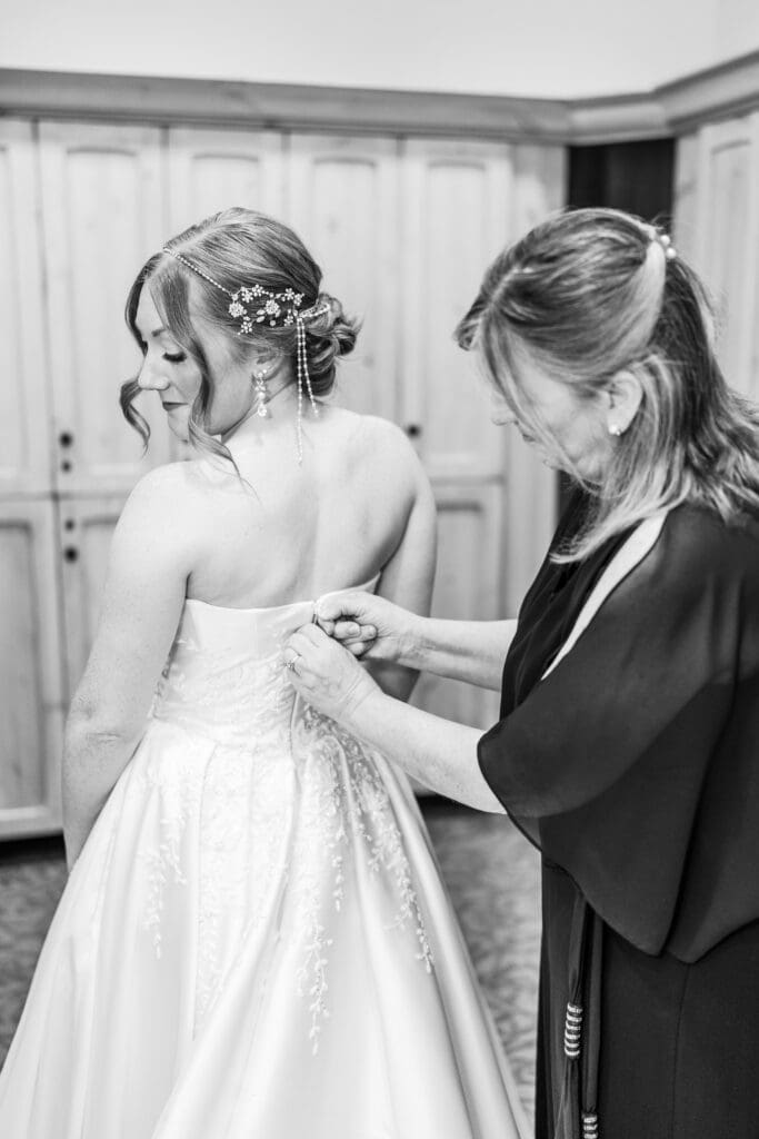 Mother of the bride zips up the bride in her wedding gown.