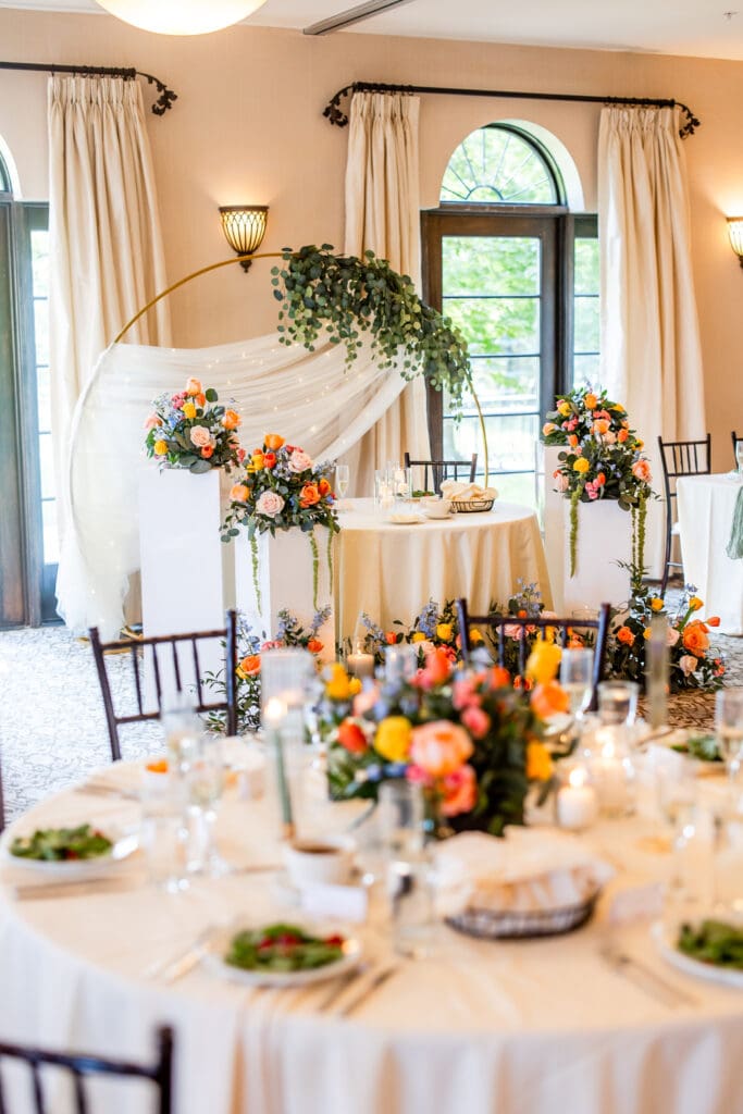 Colorful floral arrangements, a circular arch with greenery and drapery, and reception details.
