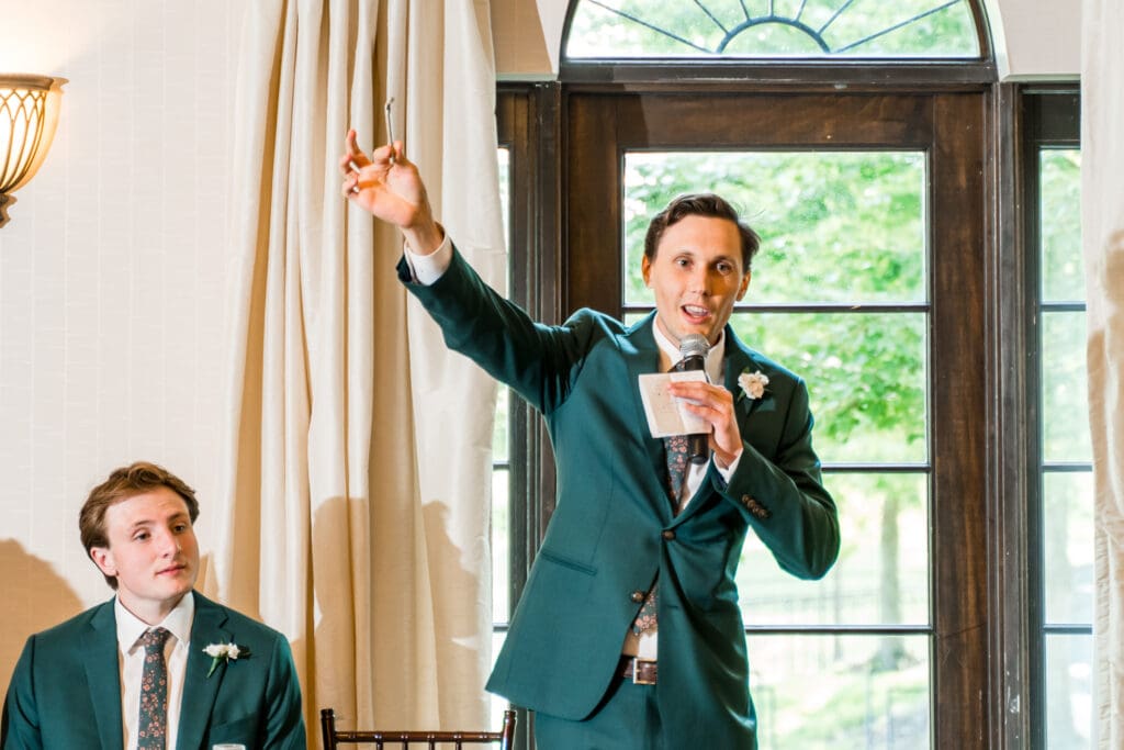 The toastmaster holds up a tool as he speaks into a microphone.