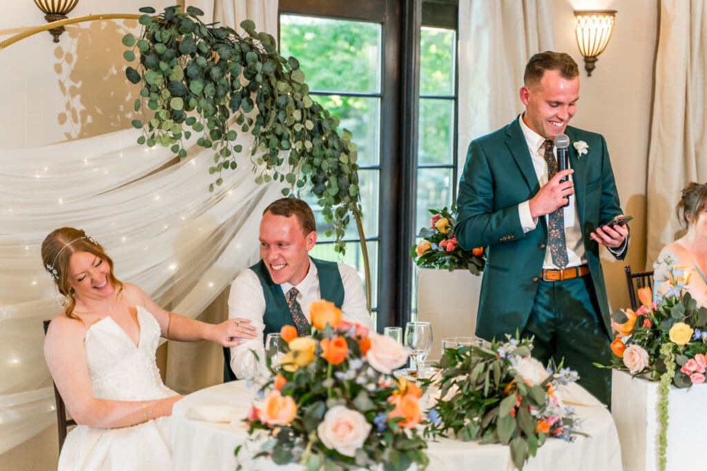 Bride and groom laugh as they listen to a groomsman's speech.