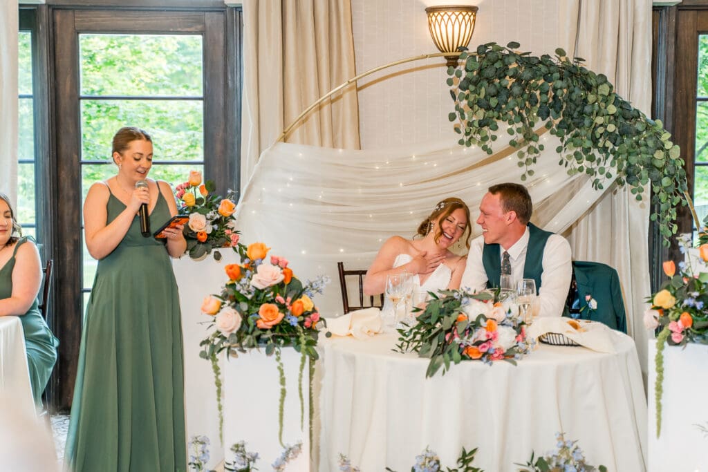 Bride and groom laugh during a bridesmaid's speech.
