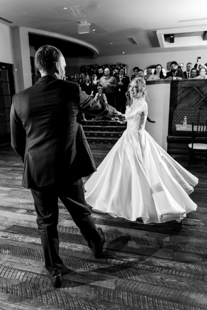 The groom spins the bride on the dance floor while their guests watch.