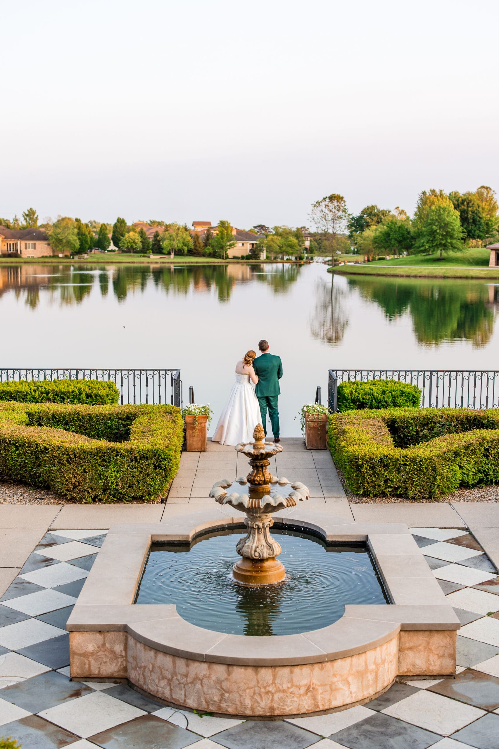 Bride and groom rests their heads together as they look out at the pond with a fountain in the foreground at the Club at Corazon.