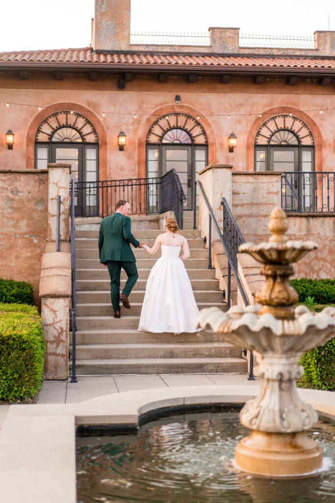 Bride and groom hold hands and walk up the stairs at a beautiful, Italian inspired venue.