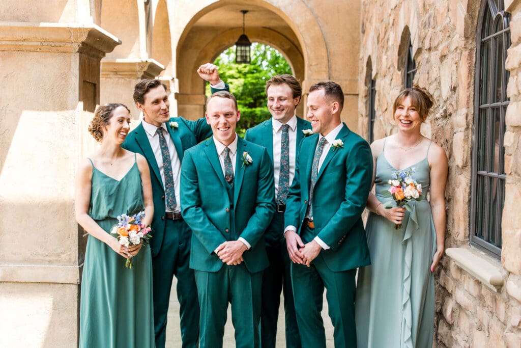 A groom and his wedding party dressed in shades of green laugh.