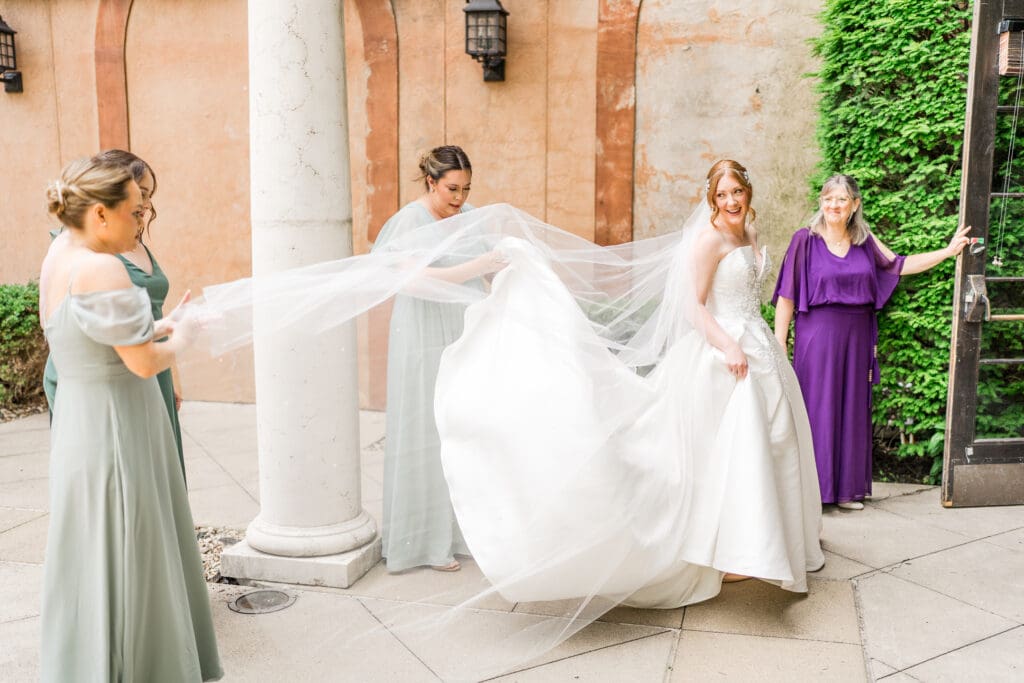 Bridesmaids hold the bride's veil as she walks inside of the Club at Corazon in Columbus, Ohio.
