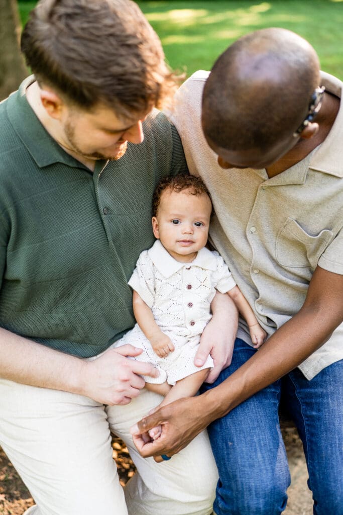 Two dads hold their baby son while sitting on a bench at Blacklick Metro Park.