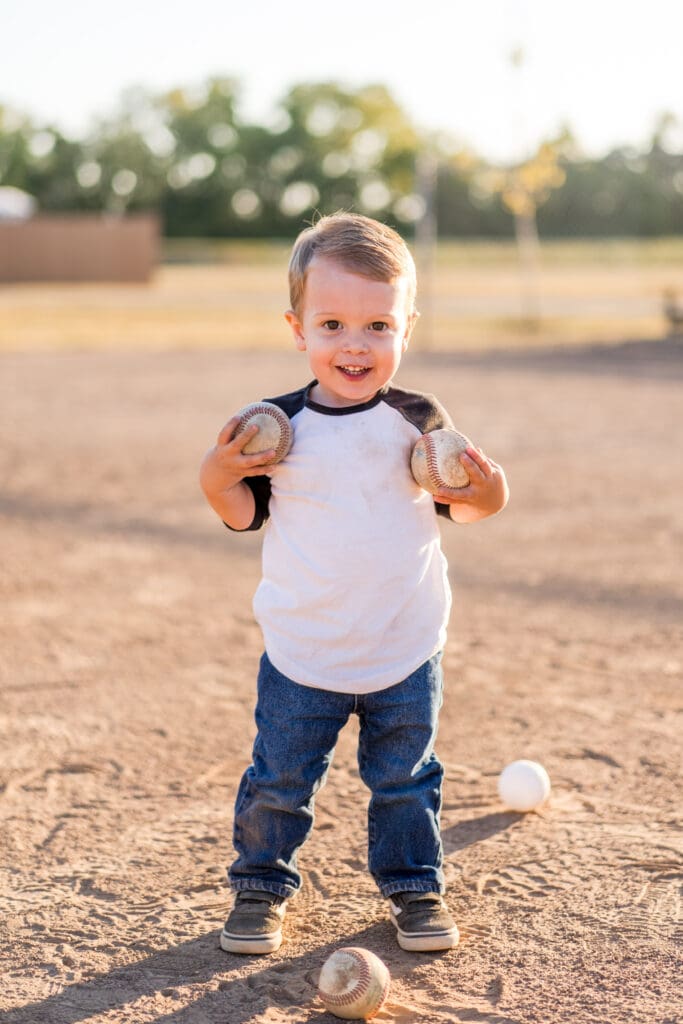 Little boy holds baseballs on a baseball field in Canal Winchester, Ohio.