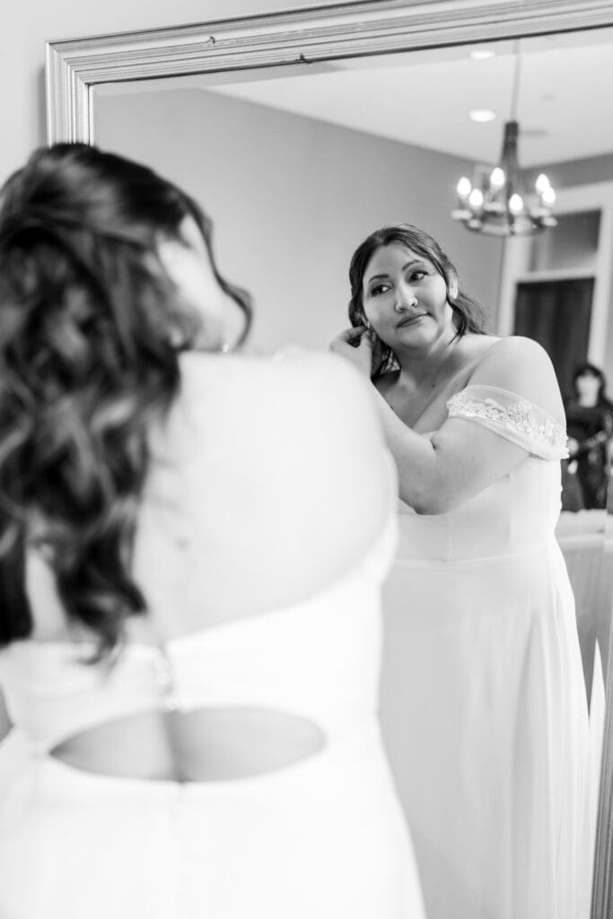 The bride looks in the mirror as she puts her earrings in.