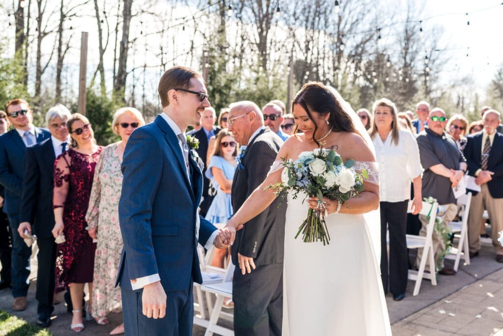 The bride takes her groom's hand during the giveaway during their ceremony