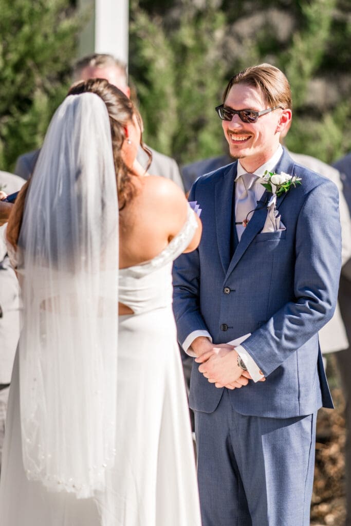 Groom smiles at his bride as she wipes away her tears during their ceremony