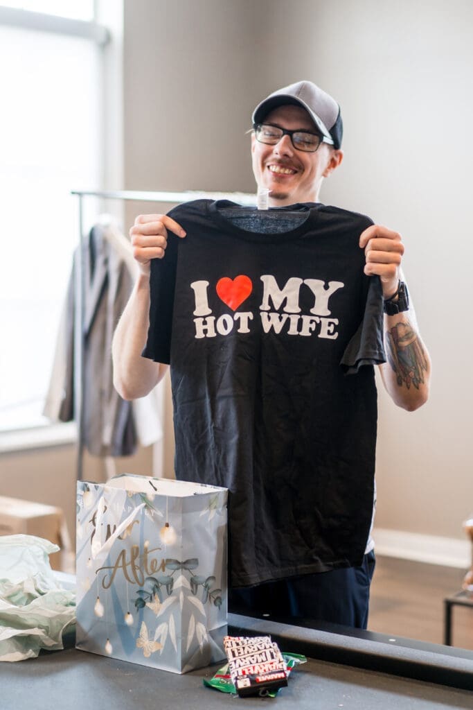 Groom holds up a "I love my hot wife" shirt from his gift from his bride.