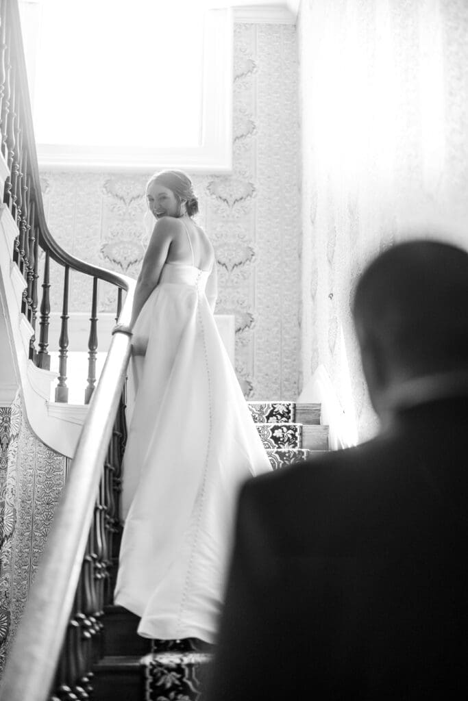 Bride looks back at her groom at the top of a staircase at the Kelton House in Columbus, Ohio
