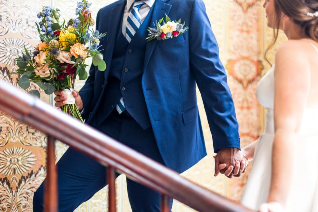 Blue and wildflower detail photo of the bride and groom holding hands at the Kelton House