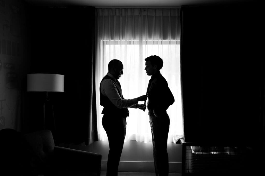 The groom fixes his brothers tie in front of a window in their hotel room at BrewDog in Columbus, Ohio.