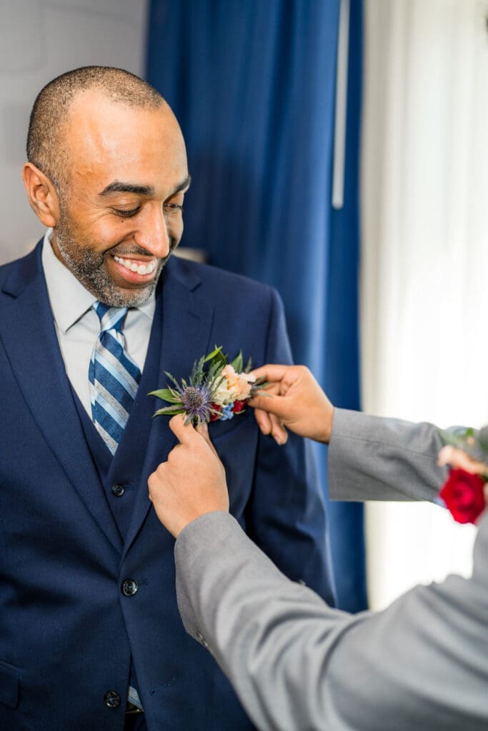 The groom's brother puts his wildflower pocket boutonniere in.