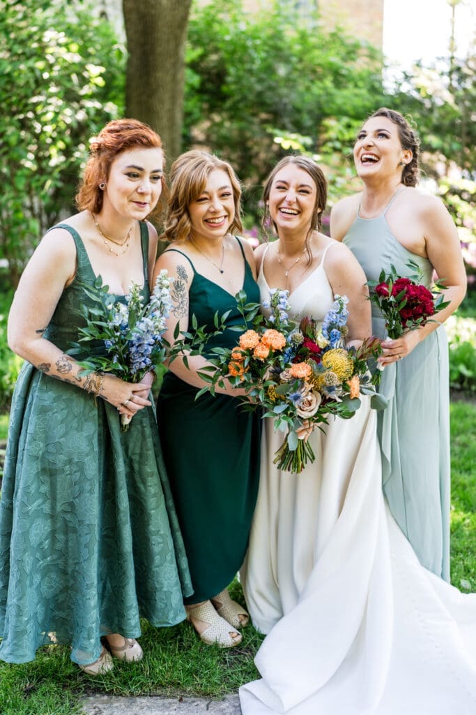 The bride and her bridesmaids dressed in shades of green and colorful wildflower bouquets