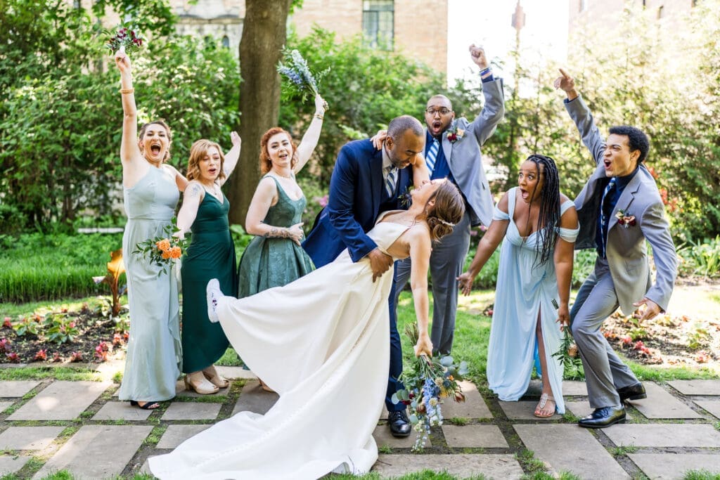 The groom dips the bride as their wedding party cheers
