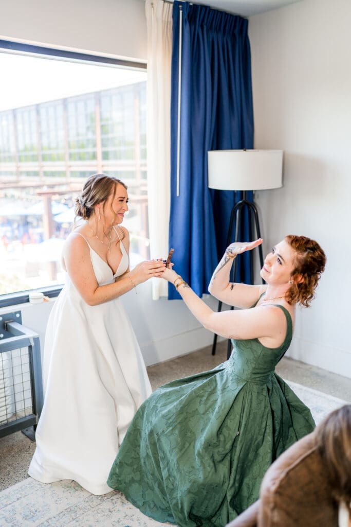 The maid of honor goofs around and pretends to propose to the bride in their hotel room.