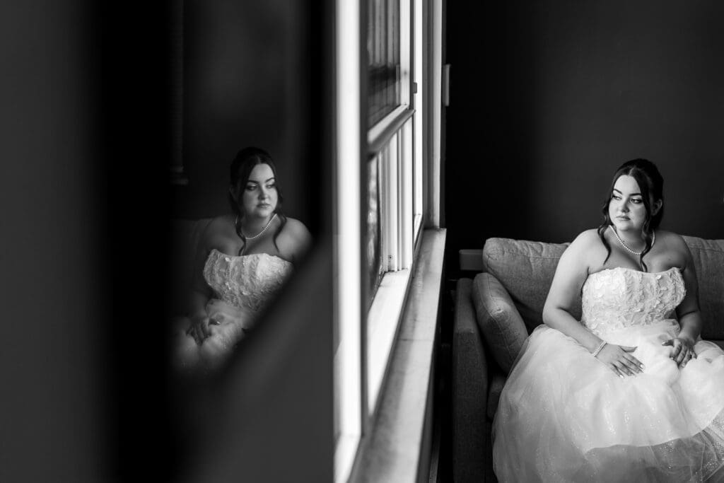 Creative bridal portrait of the bride looking out the window with a reflection of her in a photo on her wall.