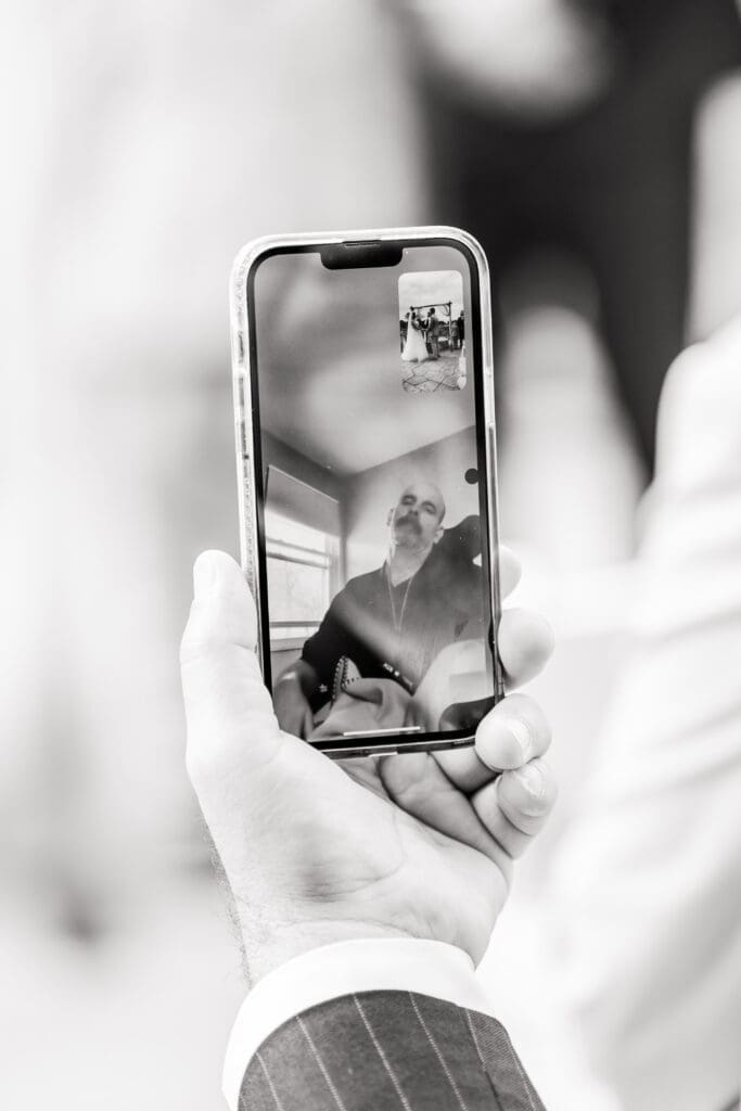 A guest holding up his phone so that the bride's dad could watch their ceremony.