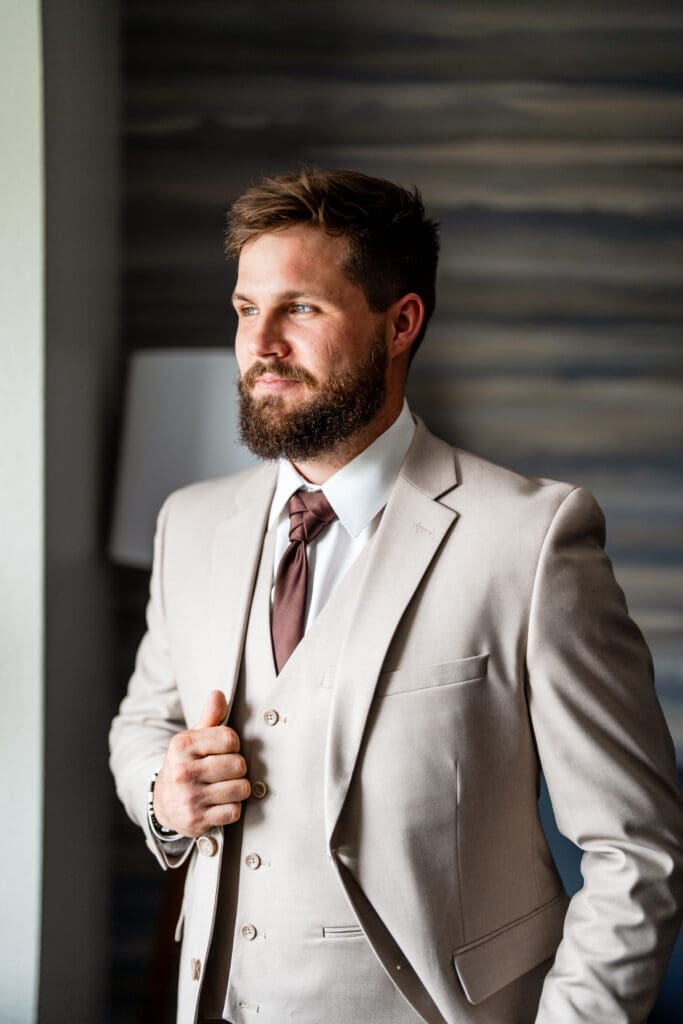 Groom portrait of the groom looking out the window in a tan suit with a brown tie in Columbus, Ohio.