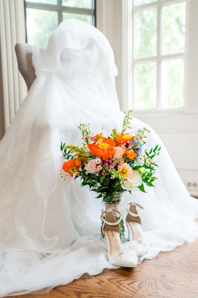 Colorful wildflower bouquet, shoes, and a wedding gown detail photo at the Dempsey Event Center